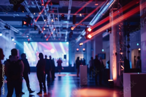 Blurred figures of attendees socializing during a lively event with dynamic stage lighting in a modern venue.