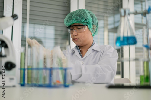 Focused researcher wearing protective lab gear carefully examines test tubes in a clinical laboratory setting.