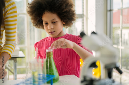 Curious child with a focus on a green solution in a test tube, experimenting in a sunny laboratory space.