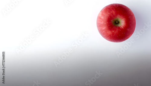 Artistic shot of a single, vibrant red apple on a white surface, located in the lower left corner, 