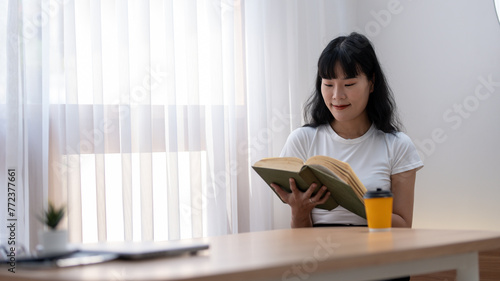 Asian women enjoy reading good books. Holding an open book and a cup of coffee on the table in a quiet cafe.