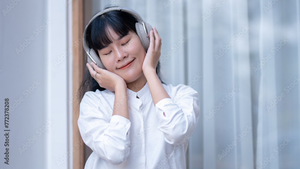Blissful Asian woman with closed eyes savoring music on wireless headphones, holding a digital tablet. Blissful Asian woman with closed eyes savoring music on wireless headphones, holding a digital tablet.