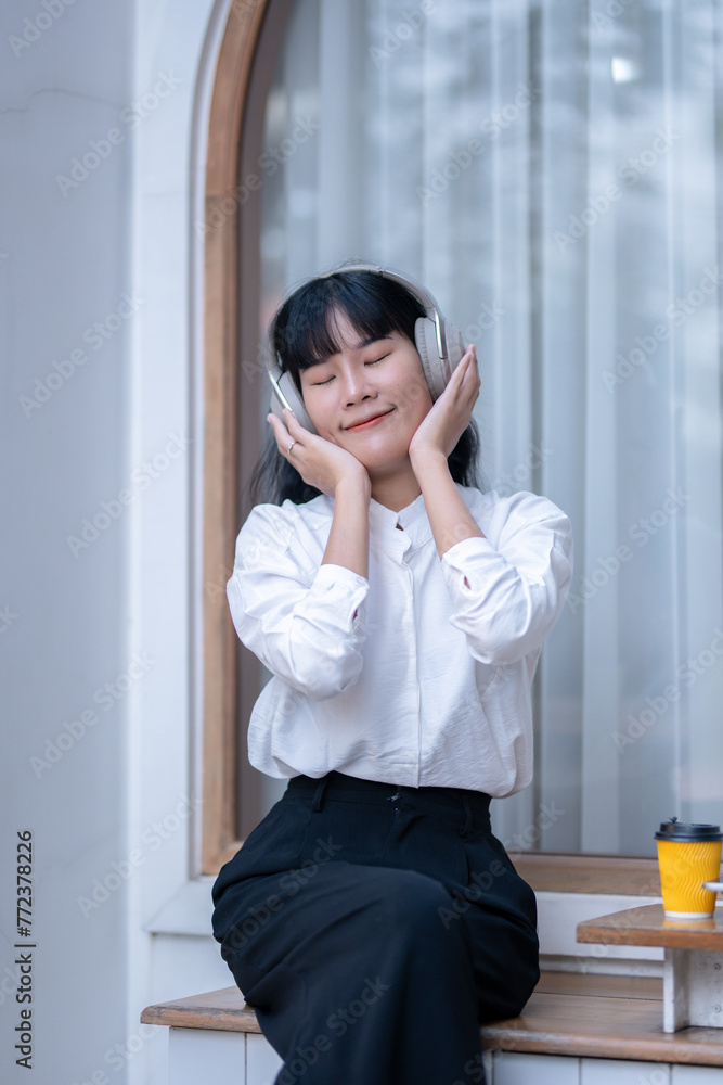 Blissful Asian woman with closed eyes savoring music on wireless headphones, holding a digital tablet. Blissful Asian woman with closed eyes savoring music on wireless headphones, holding a digital tablet.