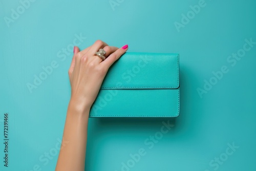 Female hand holding a turquoise clutch on a blue background photo