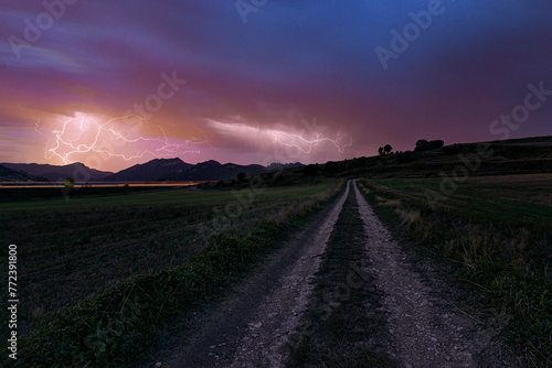 Night with an electrical storm on a rural road in the province of Burgos with the sky illuminated by lightning and the lights of the cars leaving a trail on the highway in the background