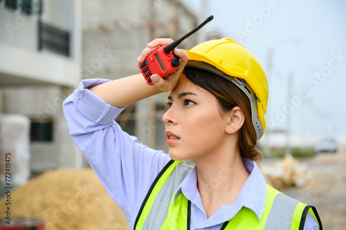 Young construction engineer woman wearing safety helmet wipes sweat on her face. Tired heat and hot at building construction site.