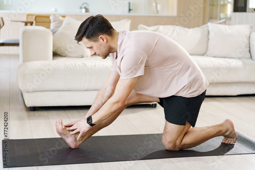 A focused individual stretches on a yoga mat, reaching towards his foot, embodying dedication in a serene home environment.