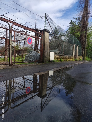 Grosse flaque d'eau avec reflextion image d'environnement, devant une imposante grille de fer local, dans un terrain de campagne urbain, vide, beauté artistique avec l'eau et la nature, illustration,  photo