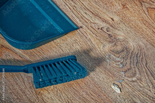 A dustpan and a brush for sweeping the floor lie on a wooden floor, there is a lot of dirt and dust on the brush, cleaning the room.
