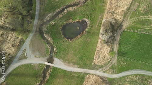 Recultivated Landscape: River, Dirt Road and Green Field. Top-down drone shot