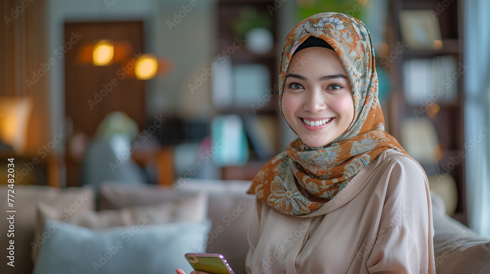 A photo of joyful asian muslim woman holding a handphone