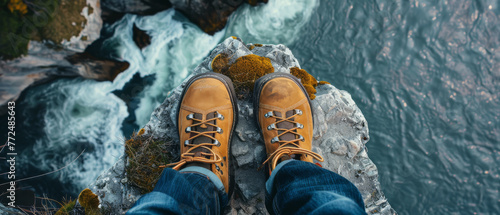 Feet in hiking boots on the cliff of a high mountain overlooking the beautiful landscape of the rocky ocean shore. Amazing view.