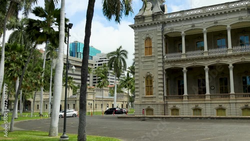 panning footage of the Iolani Palace with lush green trees, plants and grass and parked cars with clouds and blue sky in Honolulu Hawaii USA photo