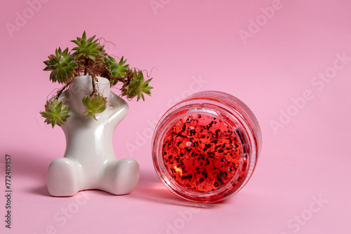 Red face mask in a cosmetic jar on a pink background 