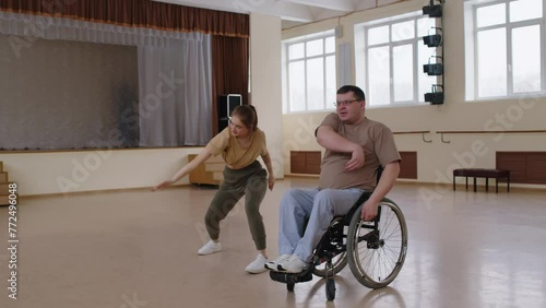 Young female teacher and man in wheelchair dancing together in studio, then hugging each other, giving high five and chatting after having successful rehearsalYoung female teacher and man in wheelchai photo