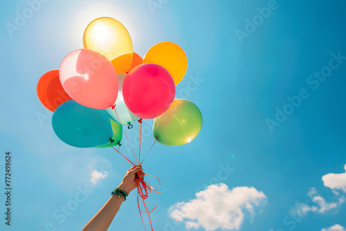 a person's hands holding colorful balloons against a bright blue sky
