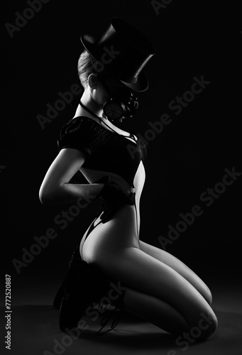 Slender woman in sexy lingerie wearing a black hat and respirator on a dark background. © Dimid