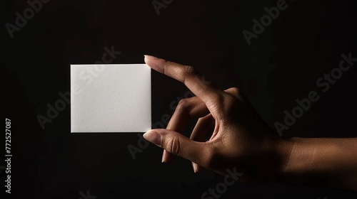 Inspired by chiaroscuro techniques, a lone female hand emerges from the shadows, grasping a pristine white card, the contrast between light and dark intensifying the impact