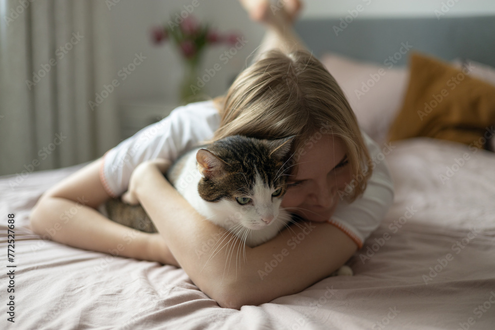 Cute Stripped White cat on owners's hands one spring day. Happy blonde 30s Girl relaxing with her pet on a bed. Cosy scene, hygge concept Cute Stripped White cat on owners's hands one spring day. Happy blonde 30s Girl relaxing with her pet on a bed. Cosy scene, hygge concept