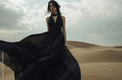 A beautiful woman with black dress, posing and standing, in sunny day, heatwave, in a desert dune, delicate modeling.