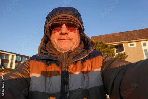 Close-up of a senior older man wearing winter coat with hood and sunglasses on a sunny winter day