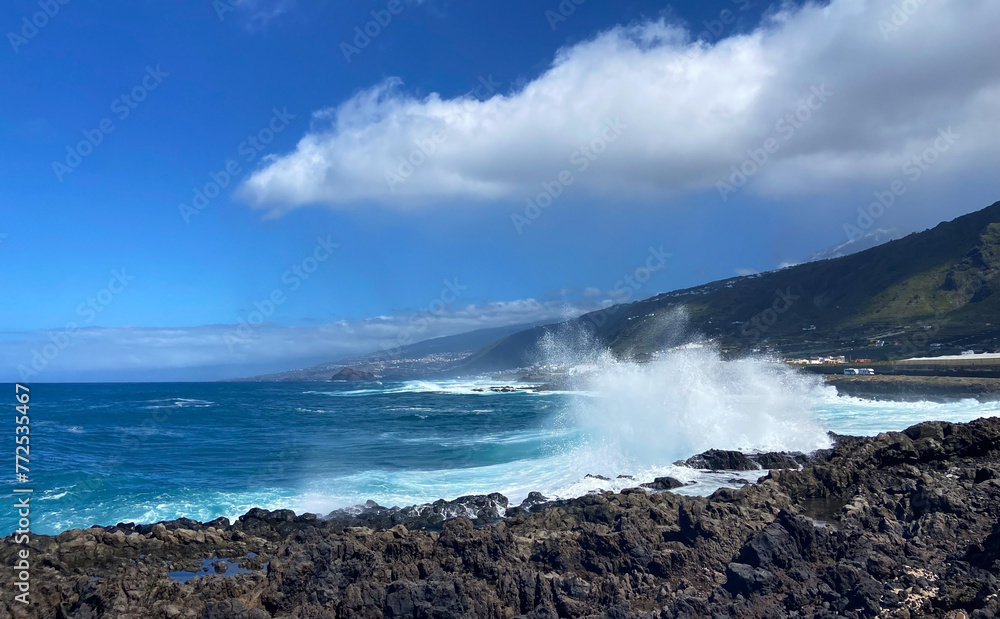 Big waves splash against black lava rock and blue Atlantic Ocean near Los Silos, Tenerife, Canary islands, Spain. Sunny spring day. Selective focus. Big waves splash against black lava rock and blue Atlantic Ocean near Los Silos, Tenerife, Canary islands, Spain. Sunny spring day. Selective focus.