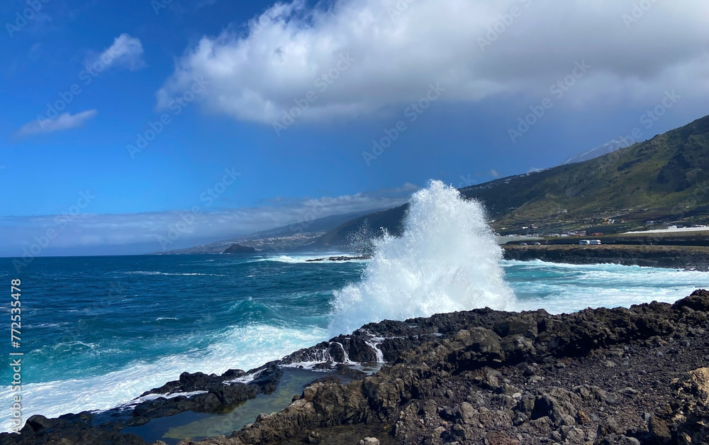 Big waves splash against black lava rock and blue  Atlantic Ocean near Los Silos, Tenerife, Canary islands, Spain. Sunny spring day. Selective focus.