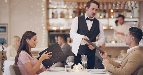 Couple on date in restaurant with menu, waiter and romantic evening together with fine dining service. Celebration of love, man and woman relax in luxury diner with server, Valentines and discussion photo