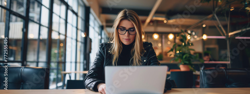 Trendy Entrepreneur at Co-Working Space. Stylish businesswoman focused on her laptop in a modern workspace.