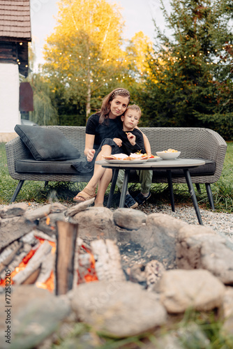 A joyful mother and son share a moment of delight on the outdoor patio, gathering around the fire pit to enjoy a meal together.