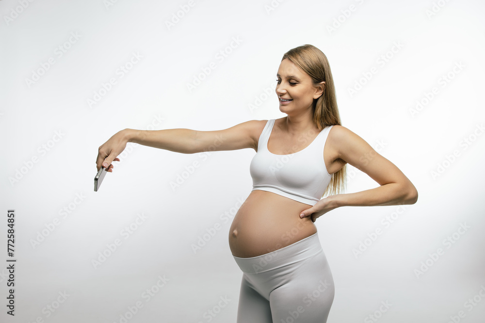 Obraz premium Pregnant woman in white top with a smartphone in hands