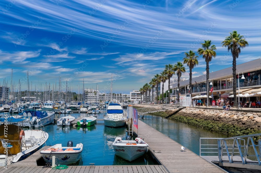 Vibrant Marina Scene with Boats, Yachts, and Palm Trees under Blue Sky in Tropical Tourist Destination