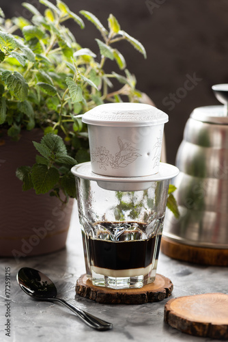 Vietnamese phin on a glass, Vietnamese coffee with condensed milk, wood stands, herbs in a pot, kettle and black spoon