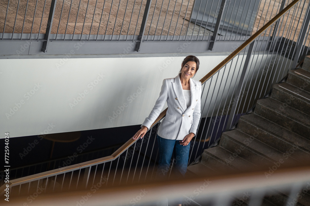 Woman in white jacket and jeans on the stairs in the office building Woman in white jacket and jeans on the stairs in the office building