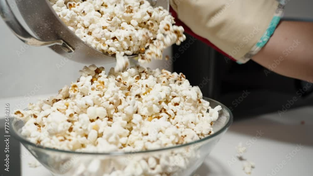 Hot homemade popcorn is poured from the pot into a large plate, which is already overflowing, causing the popcorn pile to spill over. Hot homemade popcorn is poured from the pot into a large plate, which is already overflowing, causing the popcorn pile to spill over.