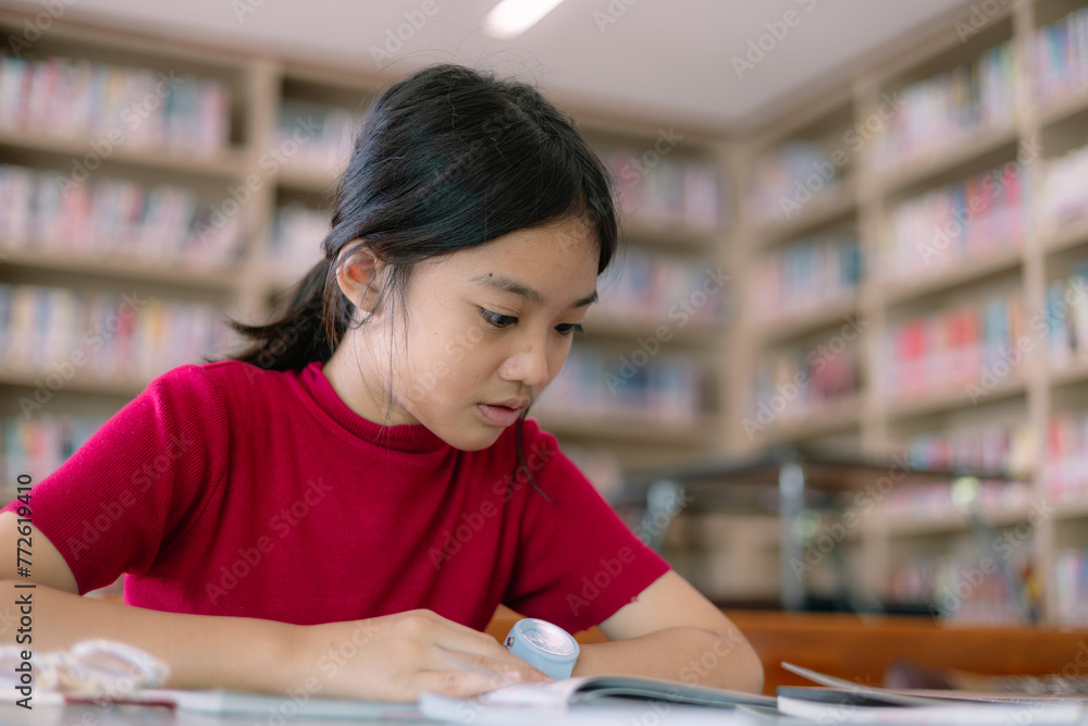 A girl is sitting at a table in a library, reading a book A girl is sitting at a table in a library, reading a book