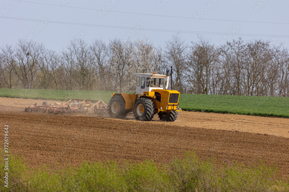 Obraz premium A tractor plows a field with seedbed cultivator in early spring