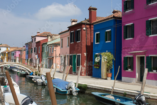 A tranquil canal in Venice, Italy, flanked by brightly colored houses and moored boats under a blue sky