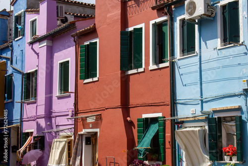 Vibrant row houses in shades of pink, blue, and purple, with contrasting green shutters, under the clear Venice sky