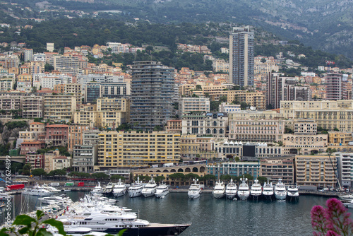 An opulent view of Monte Carlo's marina, showcasing a row of extravagant yachts moored against a backdrop of densely packed, upscale residences