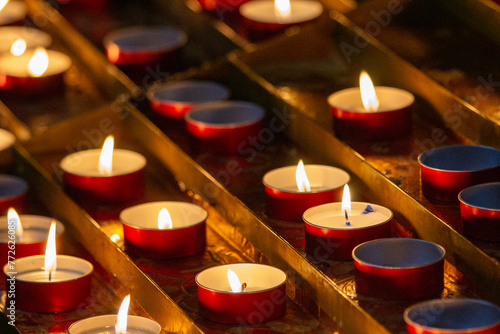 A serene display of red votive candles glowing warmly, the flickering flames offer a silent prayer and symbolize hope in the quiet of a sacred space