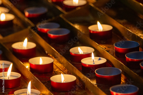 A collection of lit candles in red holders offers a tranquil sight, their flames flickering gently, evoking a sense of peace and remembrance