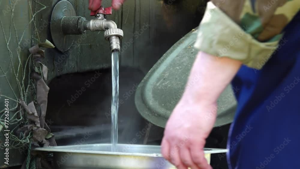 Man collects hot water from under tap into metal pelvis. Man collects hot water from under tap into metal pelvis.