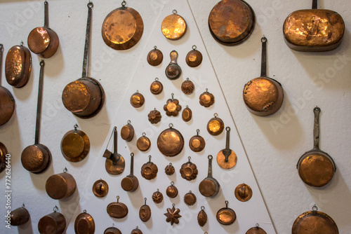 A diverse collection of copper pans and molds is artistically mounted on a wall, reflecting the light and exemplifying the charm of culinary tools photo