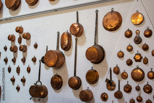An array of polished copper cookware hangs neatly on a white wall, showcasing various sizes and shapes from classic kitchenware