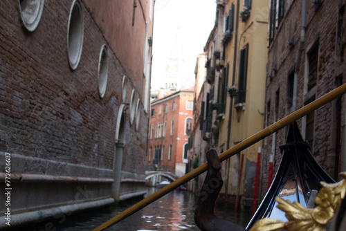 Intimate perspective from a gondola navigating a narrow, secluded canal in Venice, with historic brick buildings rising on either side.