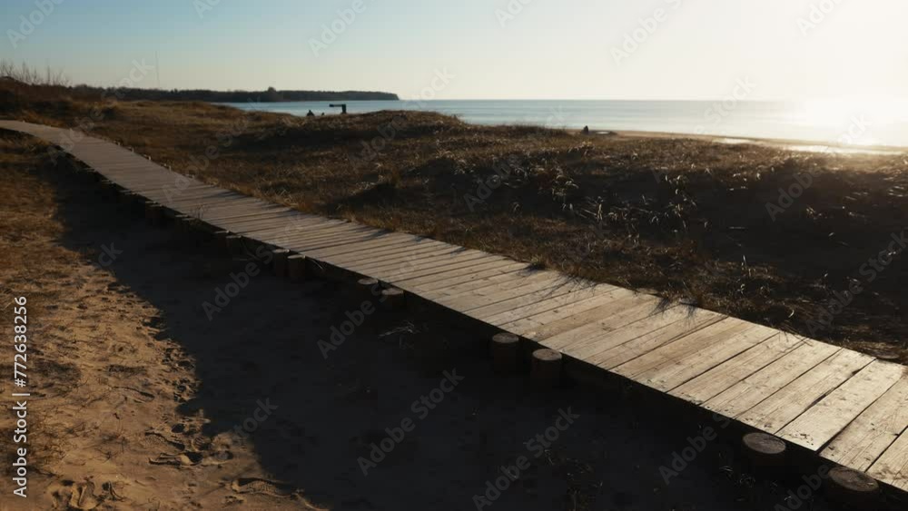 A wooden path through grassy slopes to the ocean under the sky A wooden path through grassy slopes to the ocean under the sky