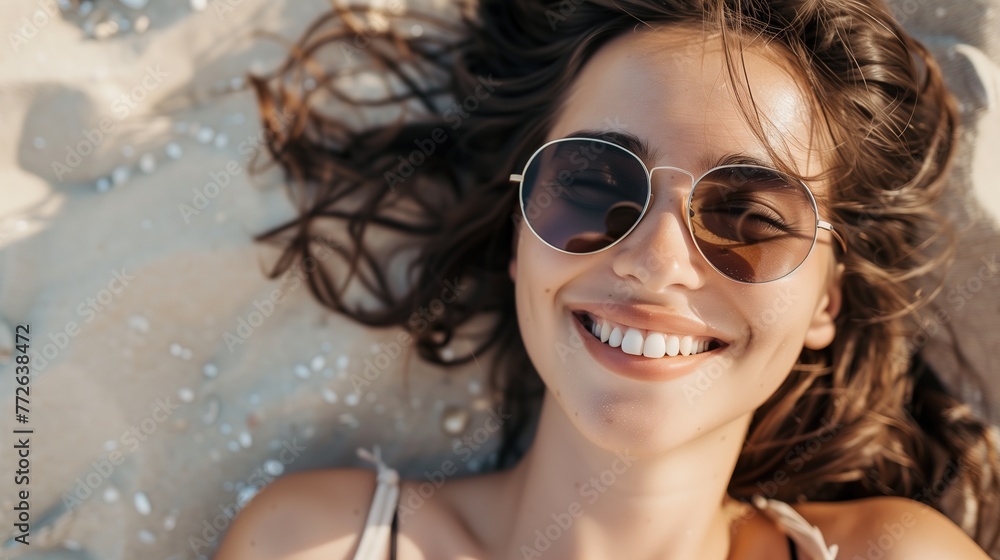 A relaxed portrait of a beautiful smiling brunette young natural woman wearing sunglasses, lounging on a sandy beach, radiating a carefree vibe ai generated high quality image