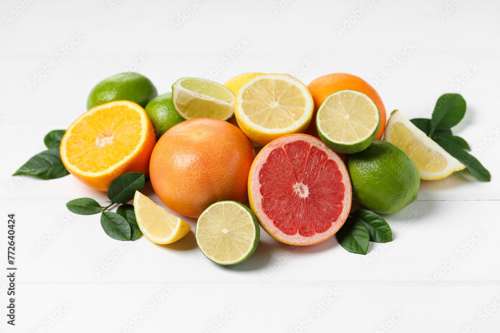 Different fresh citrus fruits and leaves on white wooden table