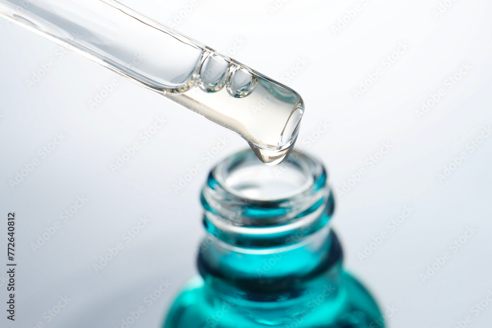 Dripping moisturizing serum from pipette into bottle on light grey background, closeup Dripping moisturizing serum from pipette into bottle on light grey background, closeup